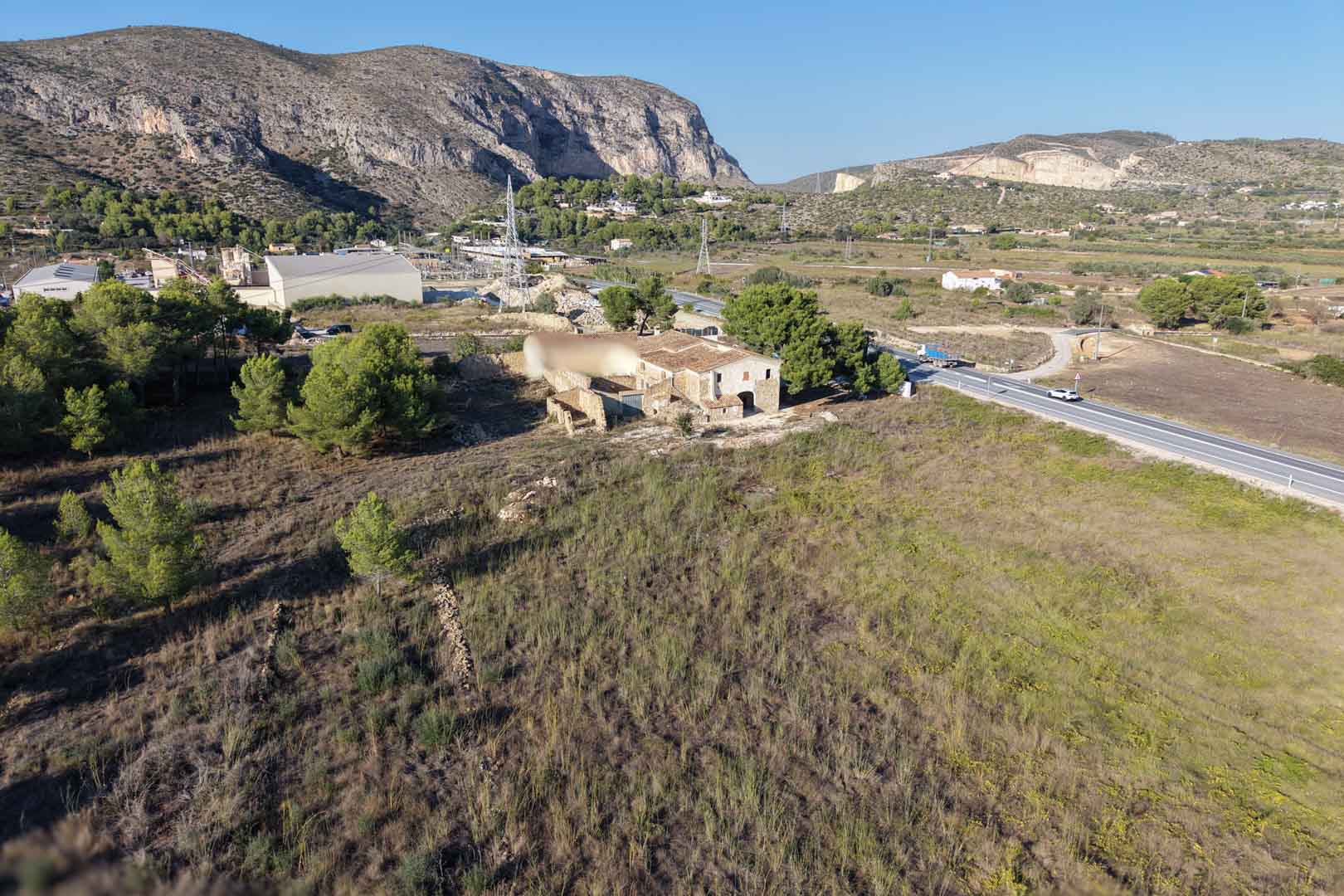 Luchtfoto van het traditionele stenen huis op een uitgestrekt vlak perceel in Teulada, met uitzicht op de bergen en de omliggende natuur.