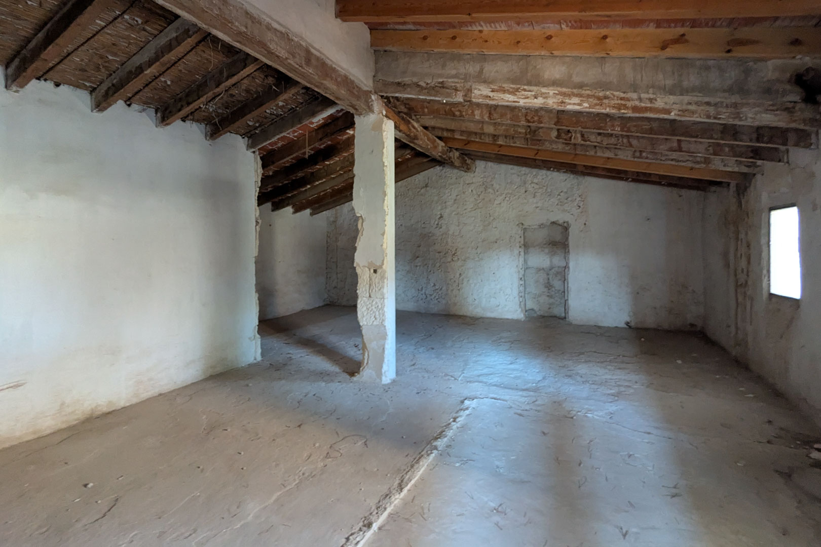 Open bovenverdieping met de originele structuur van amandelhouten balken, rieten plafonds en witgekalkte muren met een zijraam voor lichtinval.