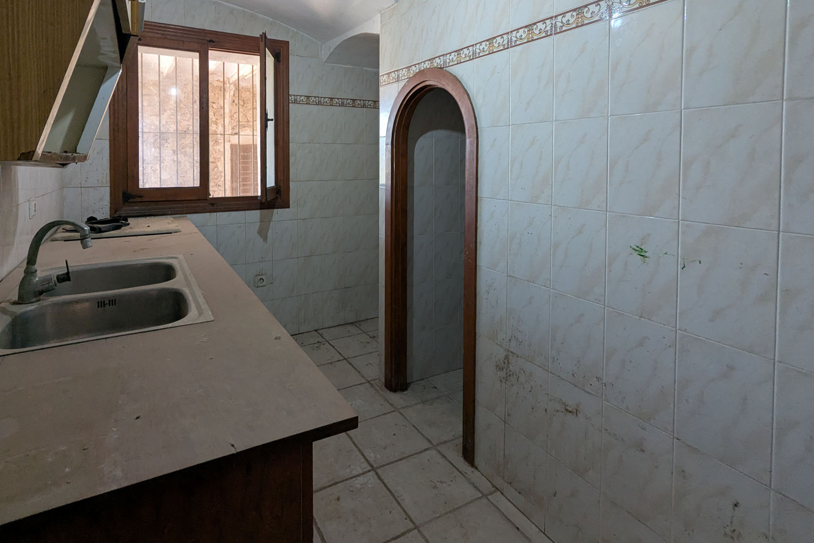 Originele rustieke keuken met dubbele roestvrijstalen spoelbak, betegelde wanden met sierrand en een houten toogdoorgang naar de rest van de woning.