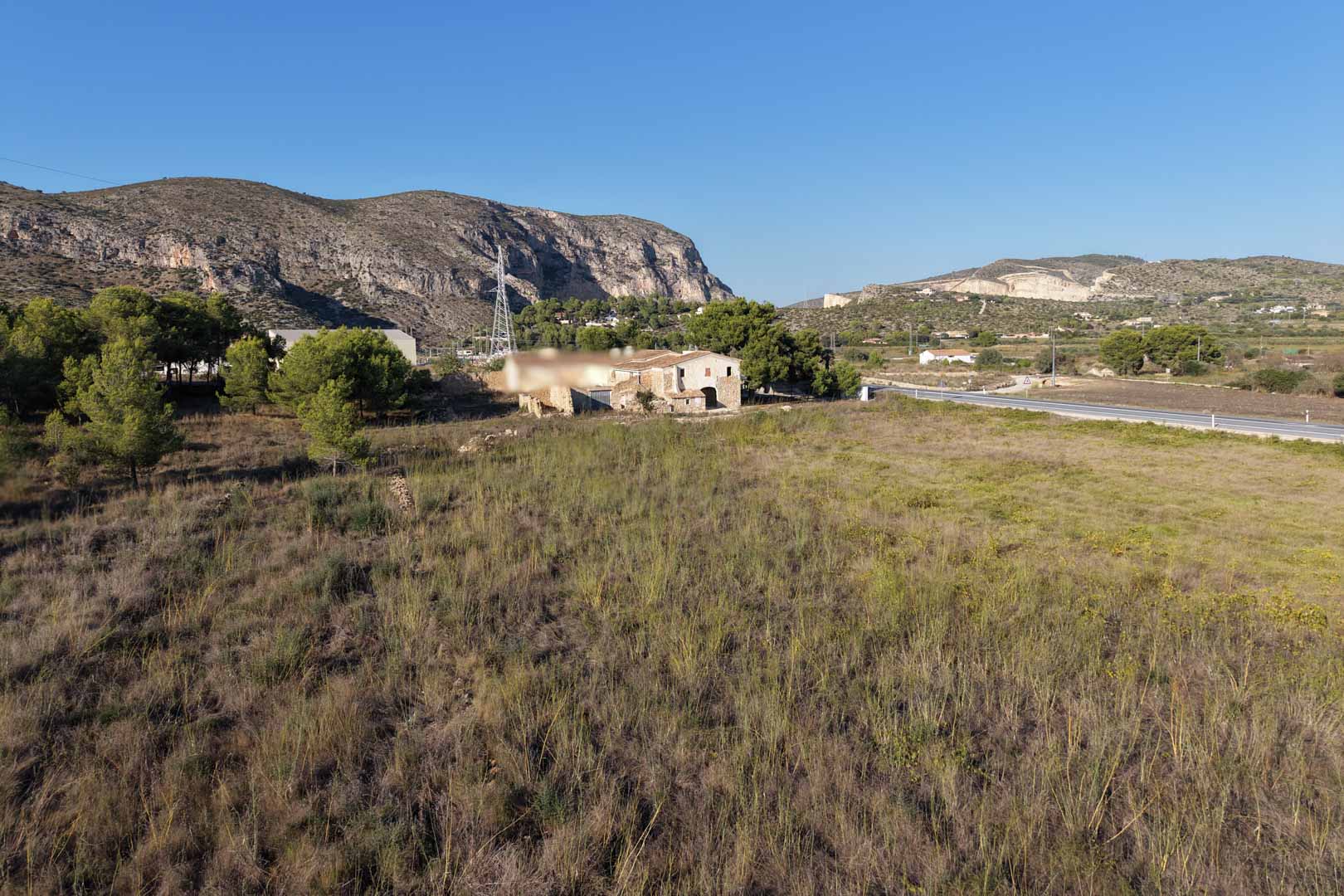 Panoramisch uitzicht op het traditionele stenen huis op een uitgestrekt landelijk perceel, omringd door mediterrane vegetatie en bergen in Teulada.
