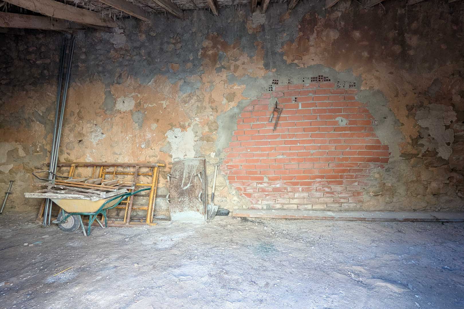 Rustiek interieur met originele stenen muren, een bakstenen gedeelte en een traditioneel plafond van houten balken en riet. De ruimte dient momenteel als opslagplaats.