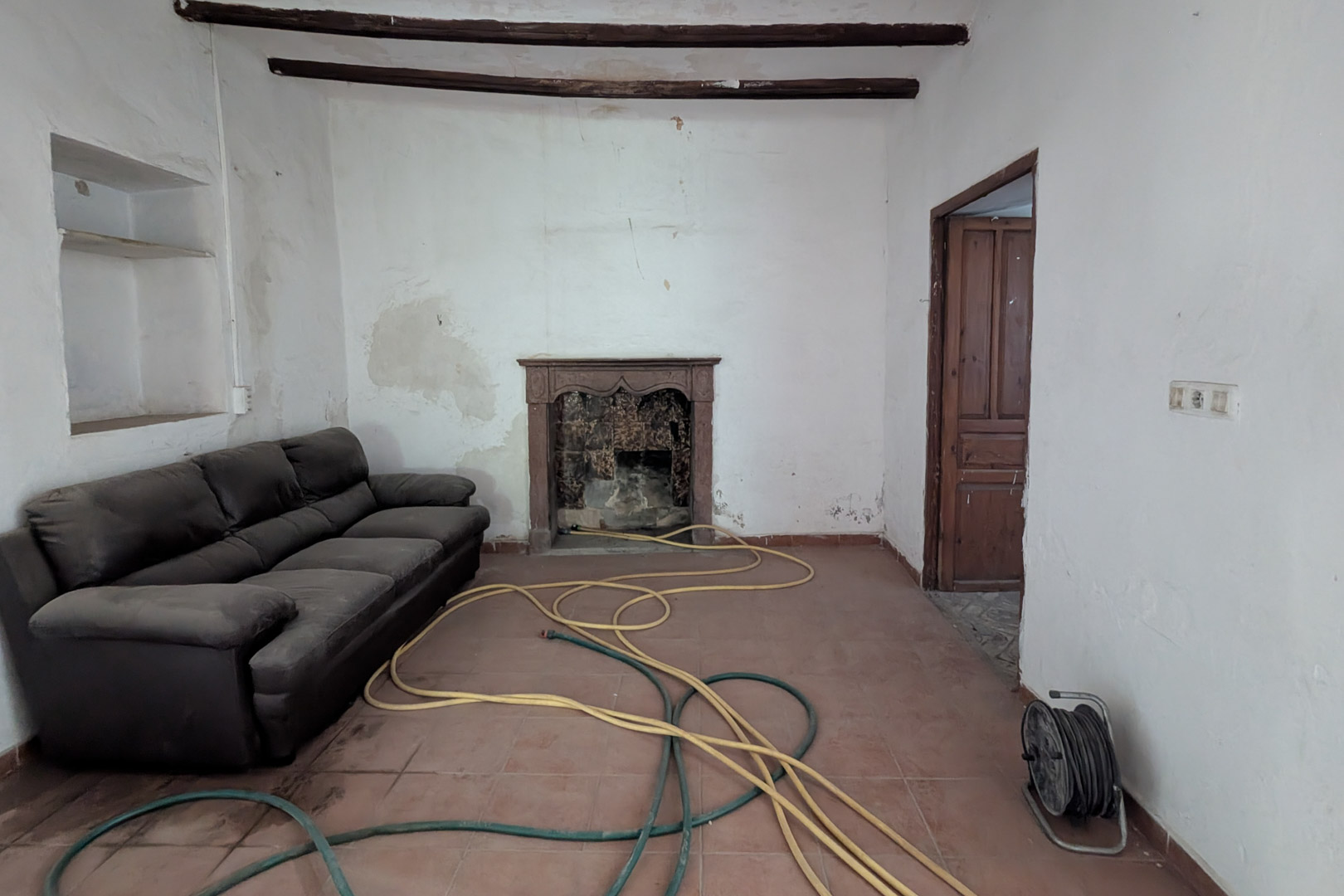 Traditionele woonkamer met originele houten balken, een terracotta tegelvloer en een authentieke open haard met een bewerkte stenen schouw.