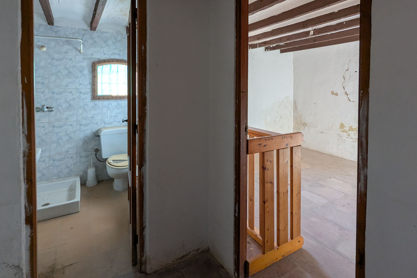 Zicht op de bovenverdieping met een betegelde badkamer en een aangrenzende kamer met houten balkenplafond en een grenen balustrade.