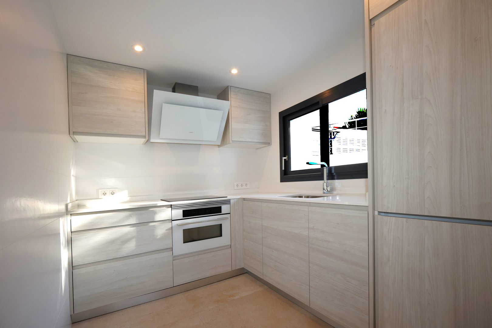Functionele keuken met lichte houten meubels, wit Silestone aanrechtblad, inductiekookplaat, Bosch oven en decoratieve afzuigkap.