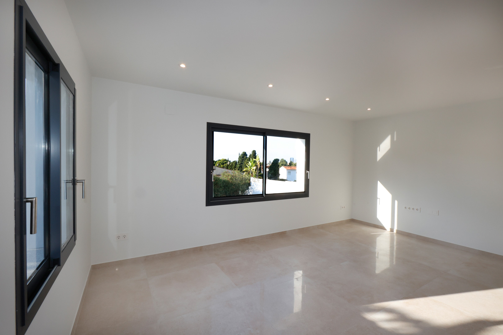 Lichte kamer met porseleinen gresvloer, antracietkleurige Technal aluminium kozijnen en geïntegreerde LED-plafondverlichting.