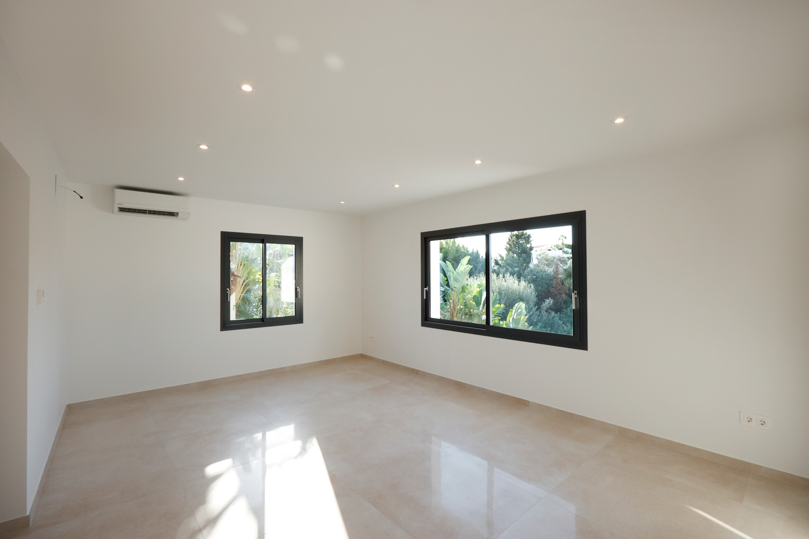 Lichte kamer met porseleinen tegelvloer, inbouw-ledverlichting, airconditioning en Technal-ramen met uitzicht op de tuin.