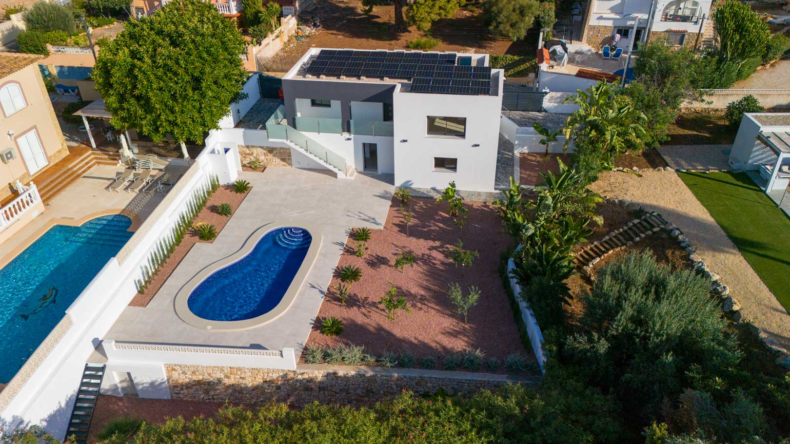 Luchtfoto van de moderne villa met zonnepanelen, een niervormig zwembad en een tuin met rood marmergrind en natuurstenen muren.