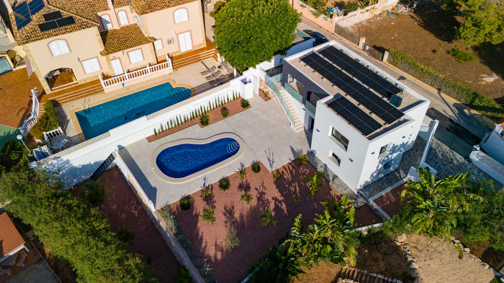 Luchtfoto van de moderne villa met zonnepanelen, een niervormig zwembad en tuin met rood marmergrind. Voorzien van glazen balustrades en natuurstenen muren.