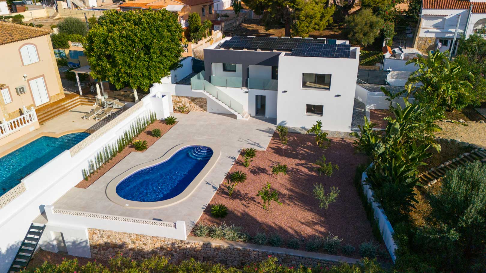 Luchtfoto van de villa met niervormig zwembad, rode marmeren grindtuin en zonnepanelen. Voorzien van glazen balustrades en natuurstenen muren.