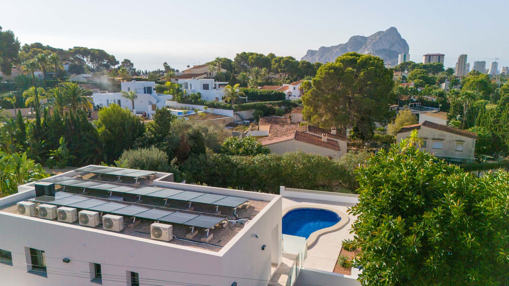 Luchtfoto van het dak met zonnepanelen en airco-units, het privézwembad en een weids uitzicht op de iconische Peñón de Ifach in Calpe.