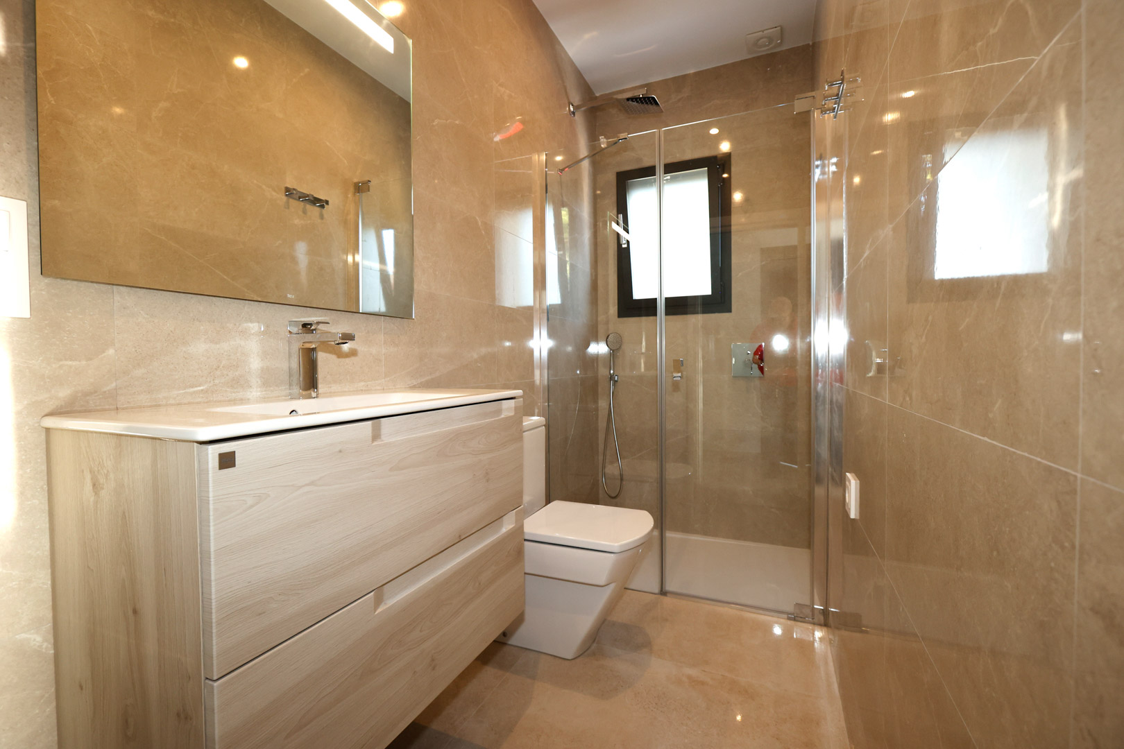 Moderne badkamer met een licht houten wastafelmeubel, wanden van porselein met marmerlook en een glazen douchecabine met chromen kranen.