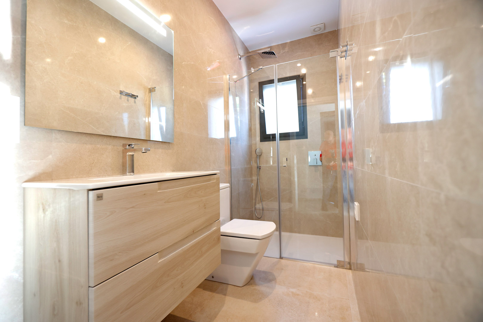 Moderne badkamer met licht houten meubel, glazen douchewand en beige porseleinen wandtegels. Voorzien van chromen kranen en geïntegreerde spiegelverlichting.