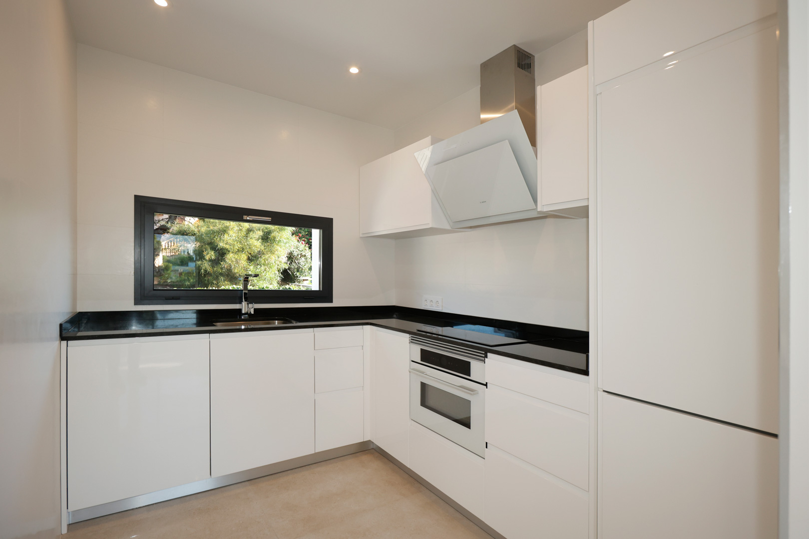 Moderne keuken met wit gelakte kasten, zwart Silestone werkblad, geïntegreerde Bosch-apparatuur en een raam met uitzicht op de tuin.