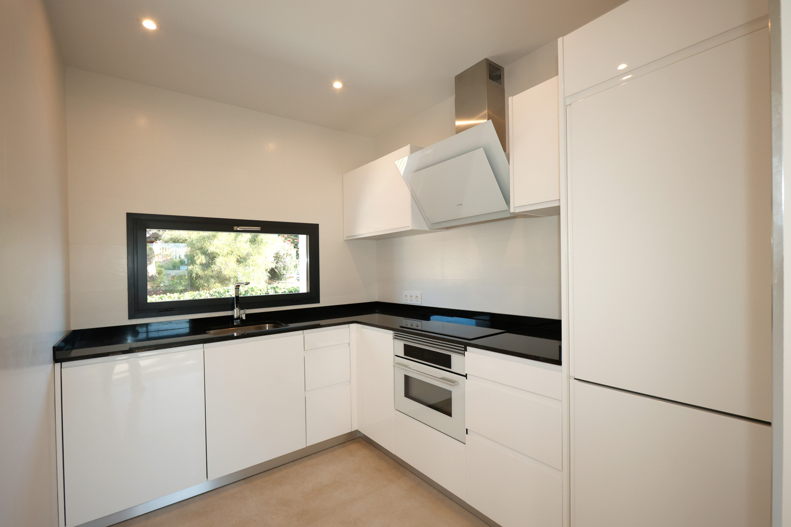 Moderne keuken met witte kasten, zwart Silestone werkblad, geïntegreerde Bosch-apparatuur en een horizontaal raam met uitzicht op de tuin.