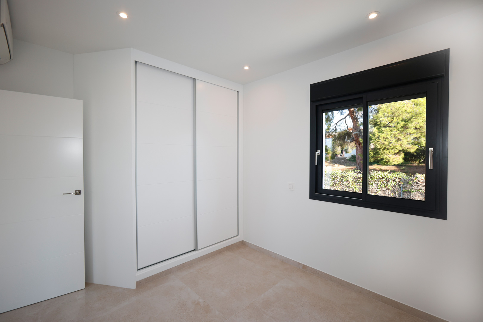 Moderne slaapkamer met witte inbouwkast met schuifdeuren, porseleinen tegelvloer en zwart aluminium raam met uitzicht op de tuin.