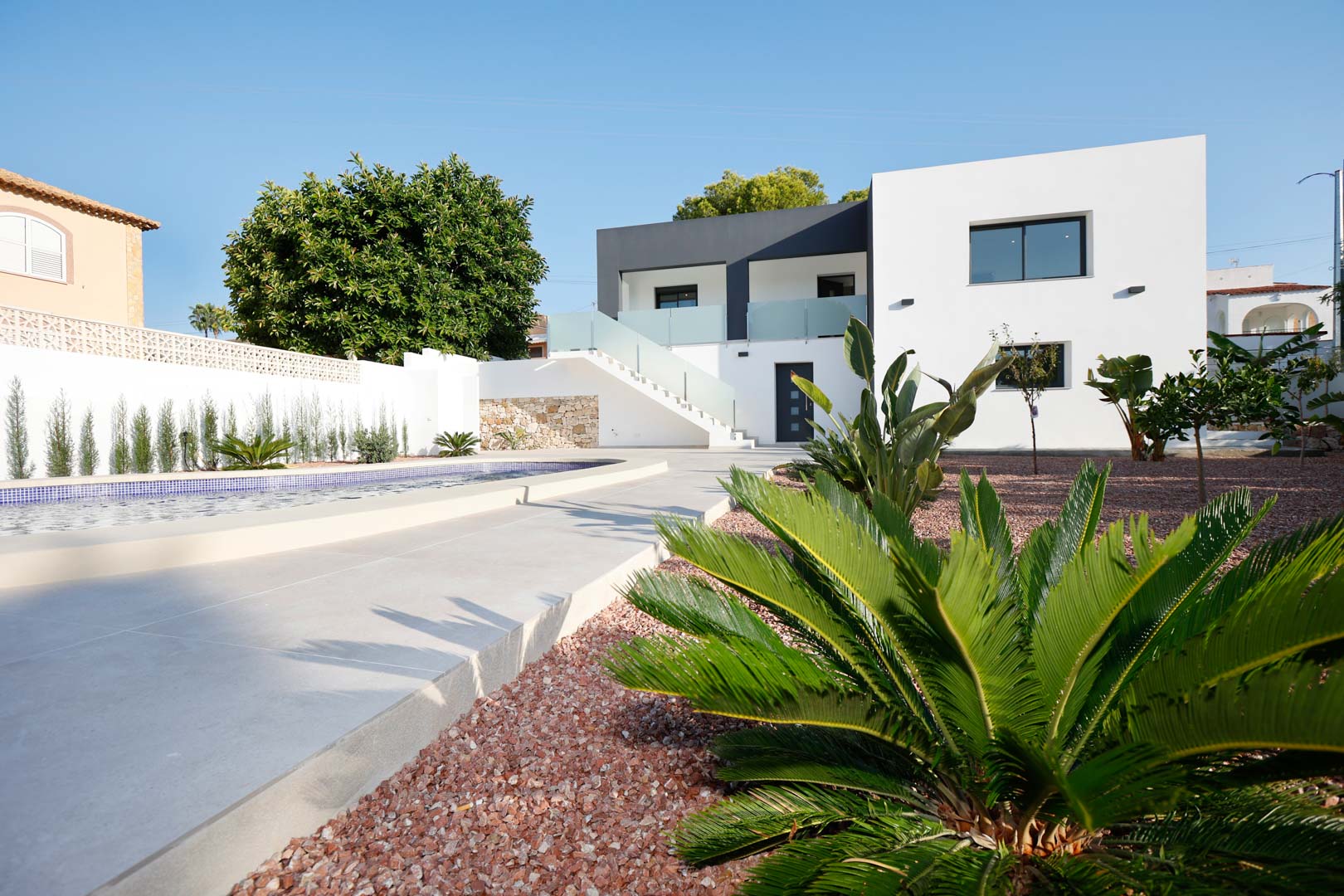 Moderne villa met twee verdiepingen, zwembad, rode marmergrindtuin en buitentrap met glazen balustrades die de onafhankelijke woningen verbindt.