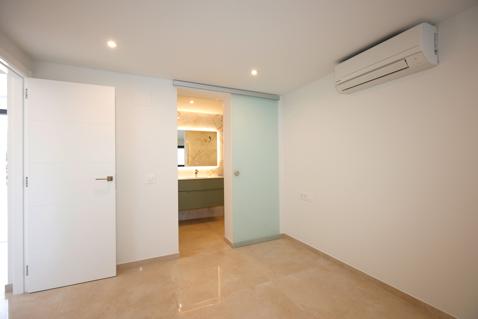 Slaapkamer met porseleinen tegelvloer, airconditioning en een matglazen schuifdeur die toegang biedt tot de moderne en-suite badkamer.