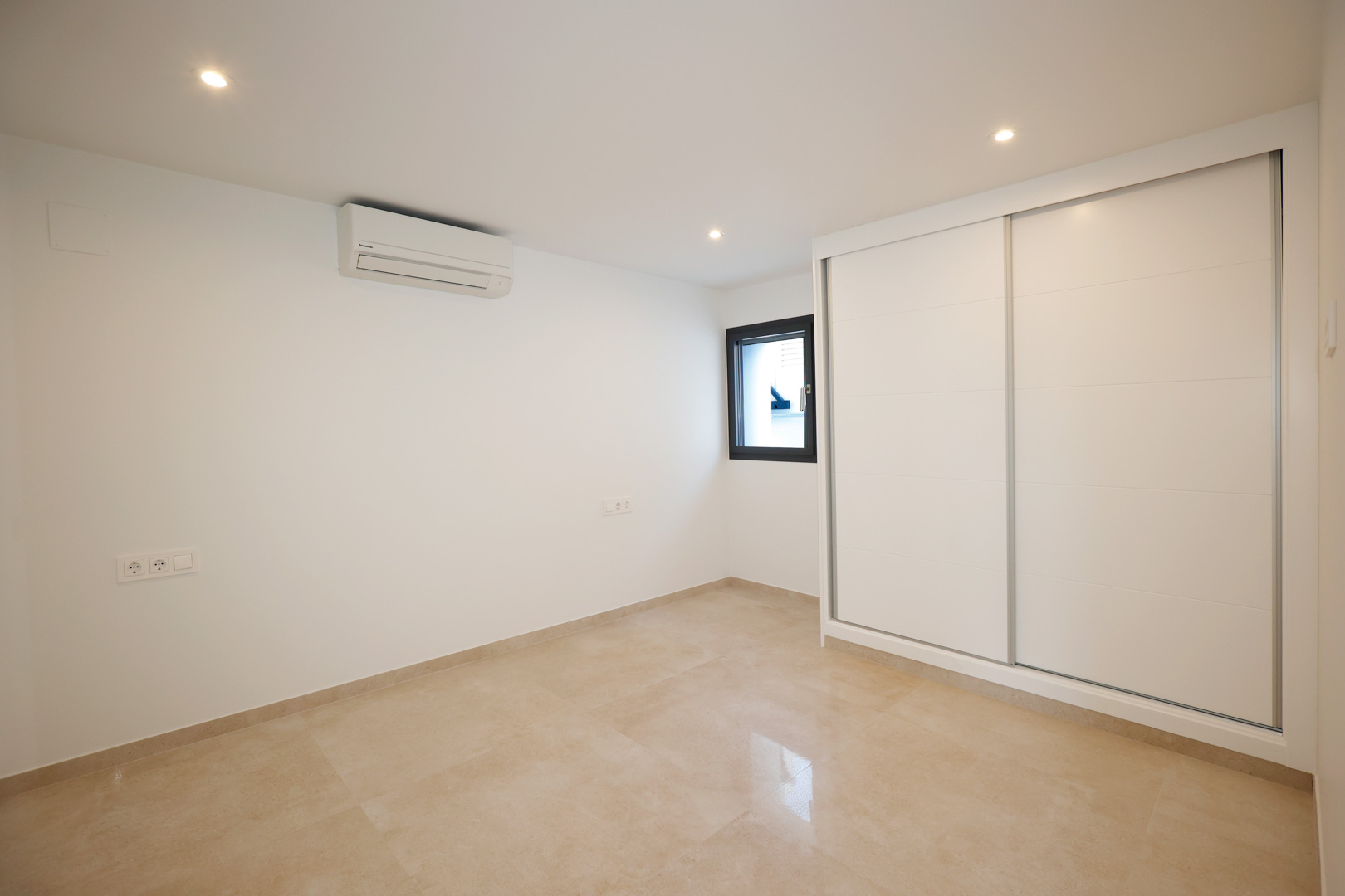 Slaapkamer met witte schuifdeurkast, porseleinen tegelvloer, split-airconditioning en in het plafond geïntegreerde ledspots.