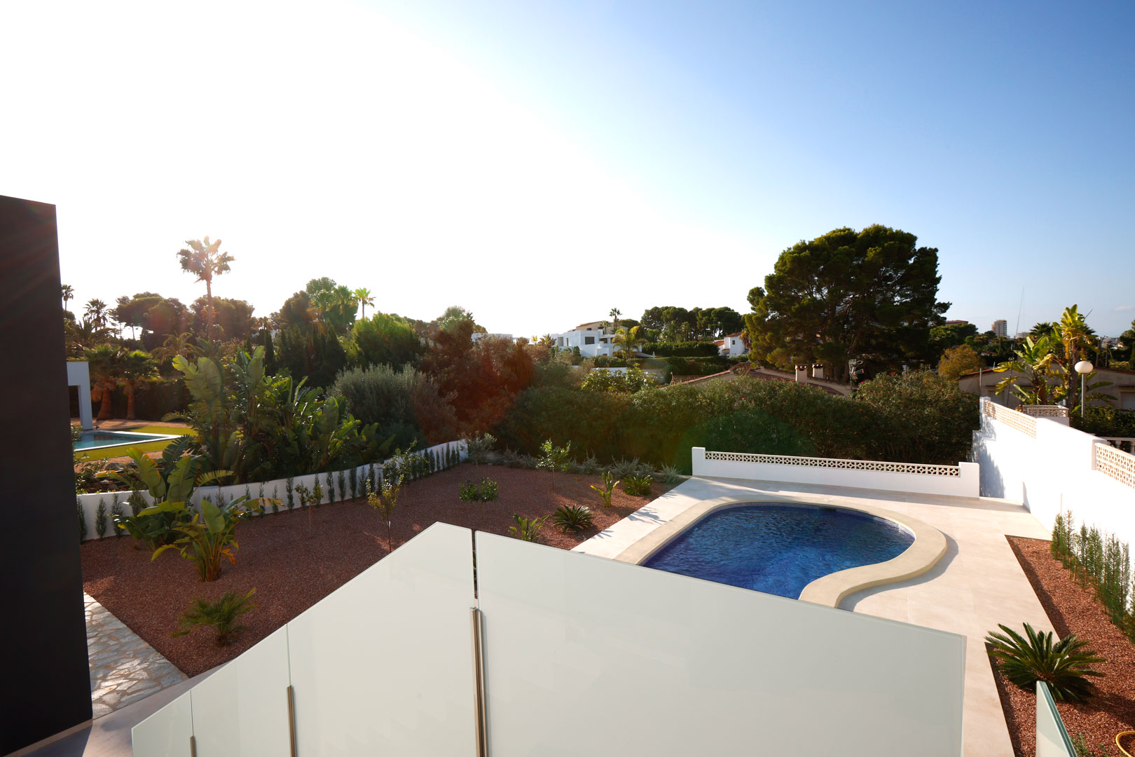 Uitzicht vanaf het boventerras met glazen balustrades op het niervormige zwembad, de tuin met rood marmergrind en de mediterrane omgeving.