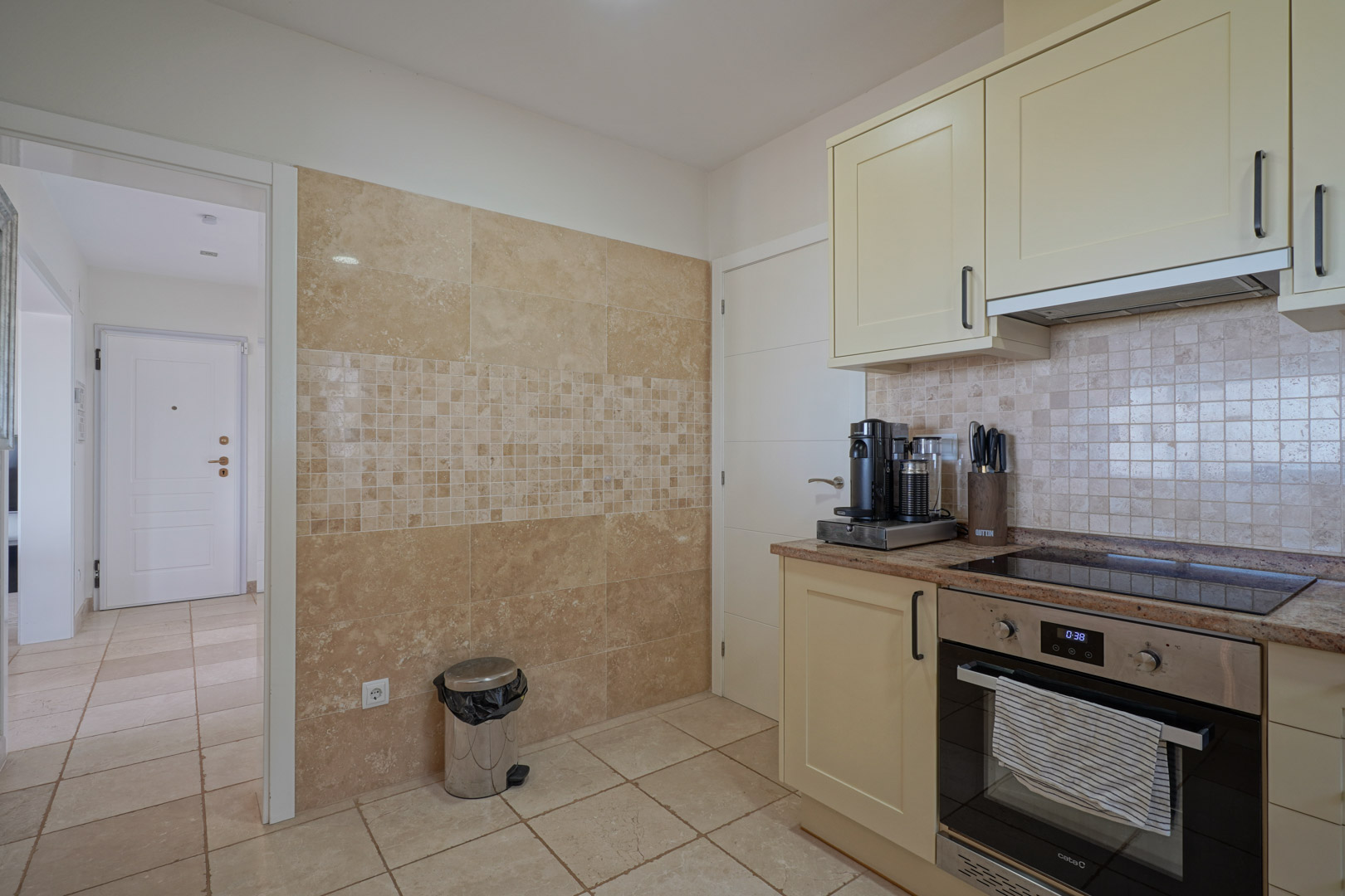 Functionele keuken met crème kasten, granieten werkblad en inbouwapparatuur. De wand is bekleed met natuursteen en voorzien van een elegant mozaïekdetail.