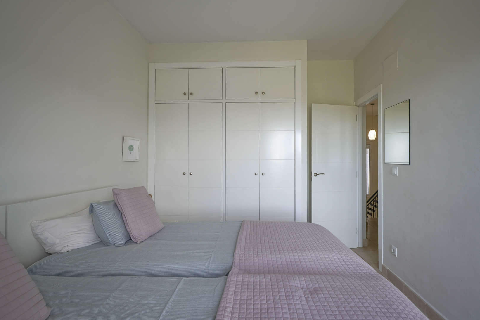 Lichte slaapkamer met kamerhoge witte inbouwkasten en een keramische tegelvloer. Het minimalistische ontwerp biedt een rustige en functionele sfeer.