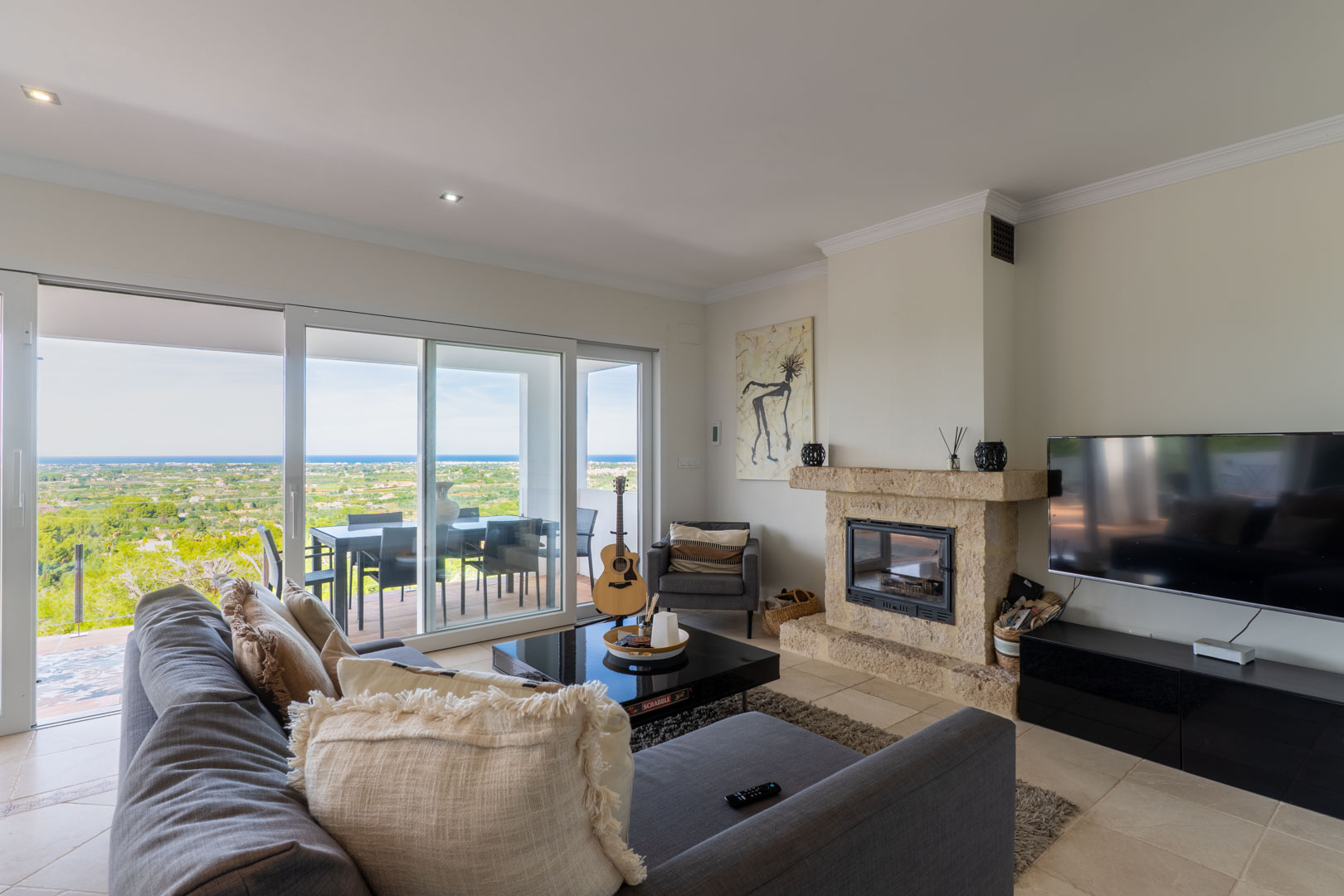 Lichte woonkamer met een natuurstenen open haard, grote glazen schuifdeuren naar het terras en panoramisch uitzicht op de Middellandse Zee en de natuur.