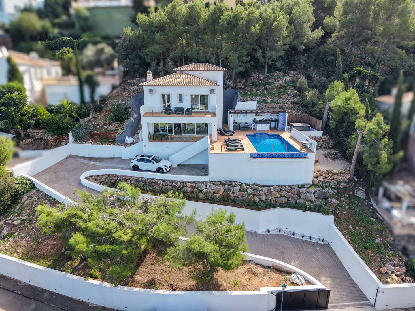 Luchtfoto van de mediterrane villa met overloopzwembad, buitenkeuken en ruime terrassen, gelegen op een bebost perceel in de exclusieve wijk La Sella.