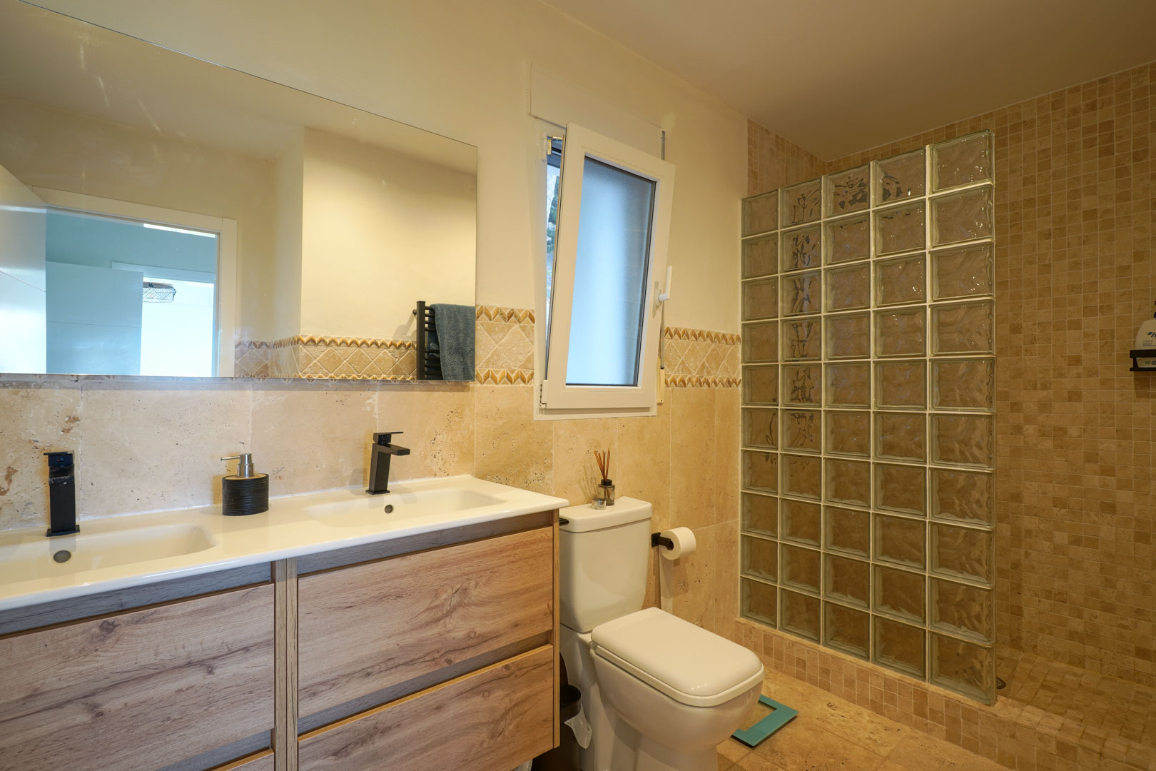 Moderne badkamer met dubbel houten wastafelmeubel, zwarte kranen en een inloopdouche met een wand van glasblokken.
