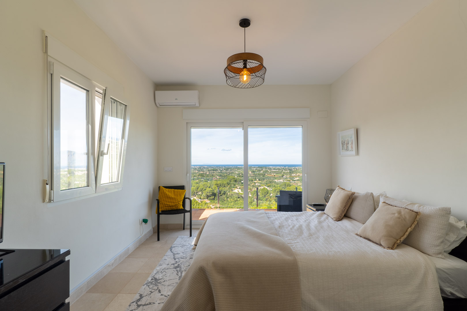 Slaapkamer met toegang tot het terras en panoramisch uitzicht op zee. Voorzien van airconditioning, tegelvloer en een grote glazen schuifdeur.