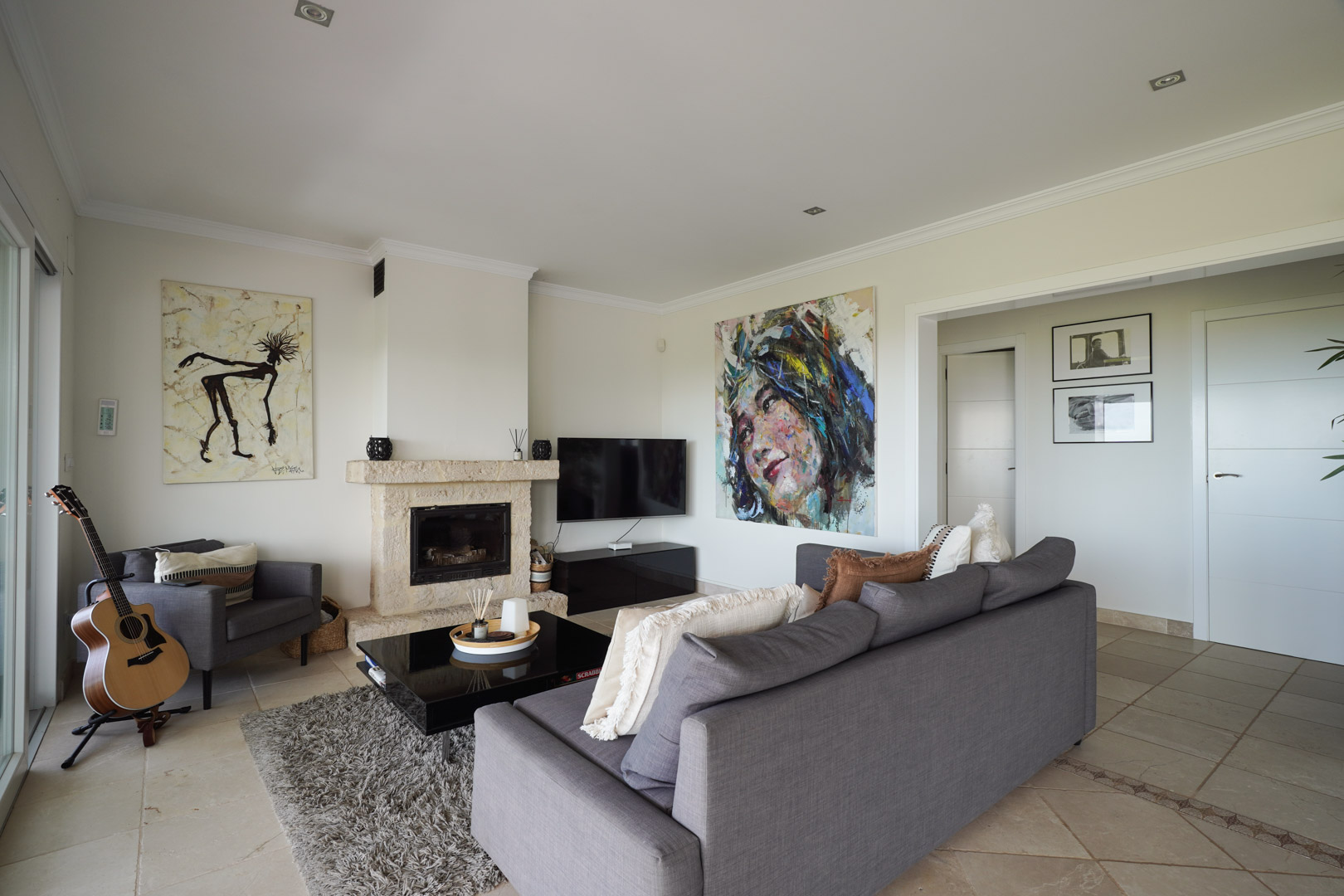 Woonkamer met natuurstenen schouw, grijze meubels en tegelvloer met sierrand. Moderne kunst en inbouwspots versterken de elegante uitstraling van de ruimte.