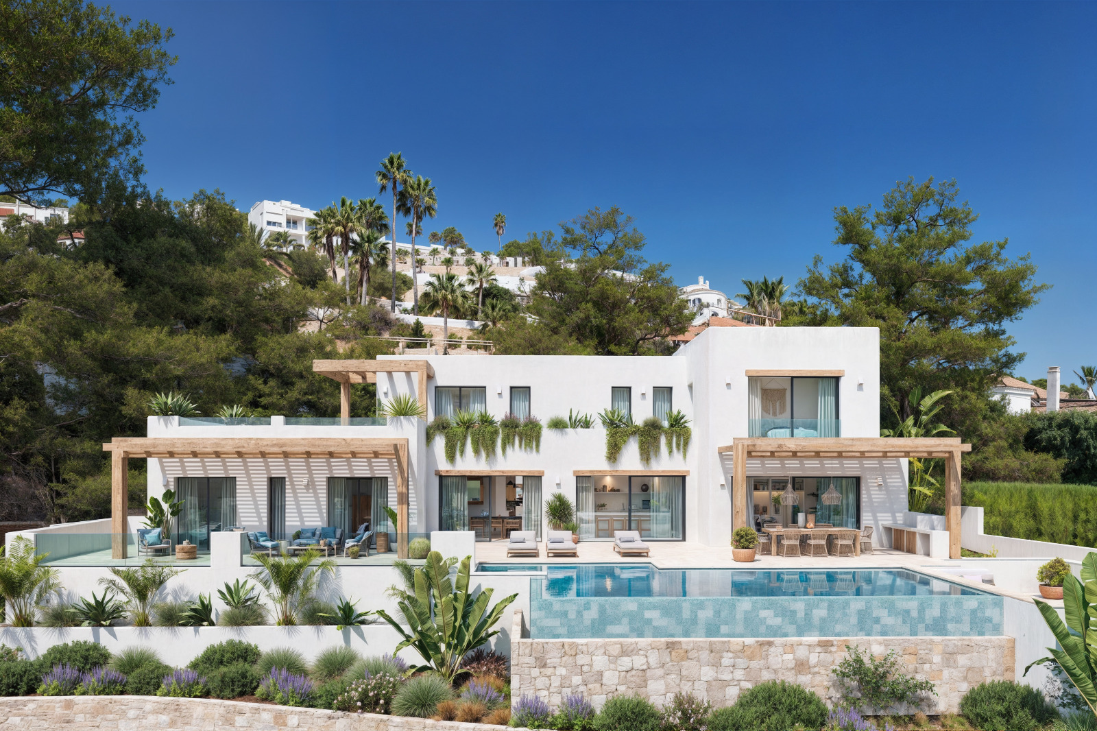 Buitenaanzicht van de villa met witte gevels, houten pergola's, een overloopzwembad en een mediterrane tuin met natuurstenen muren.