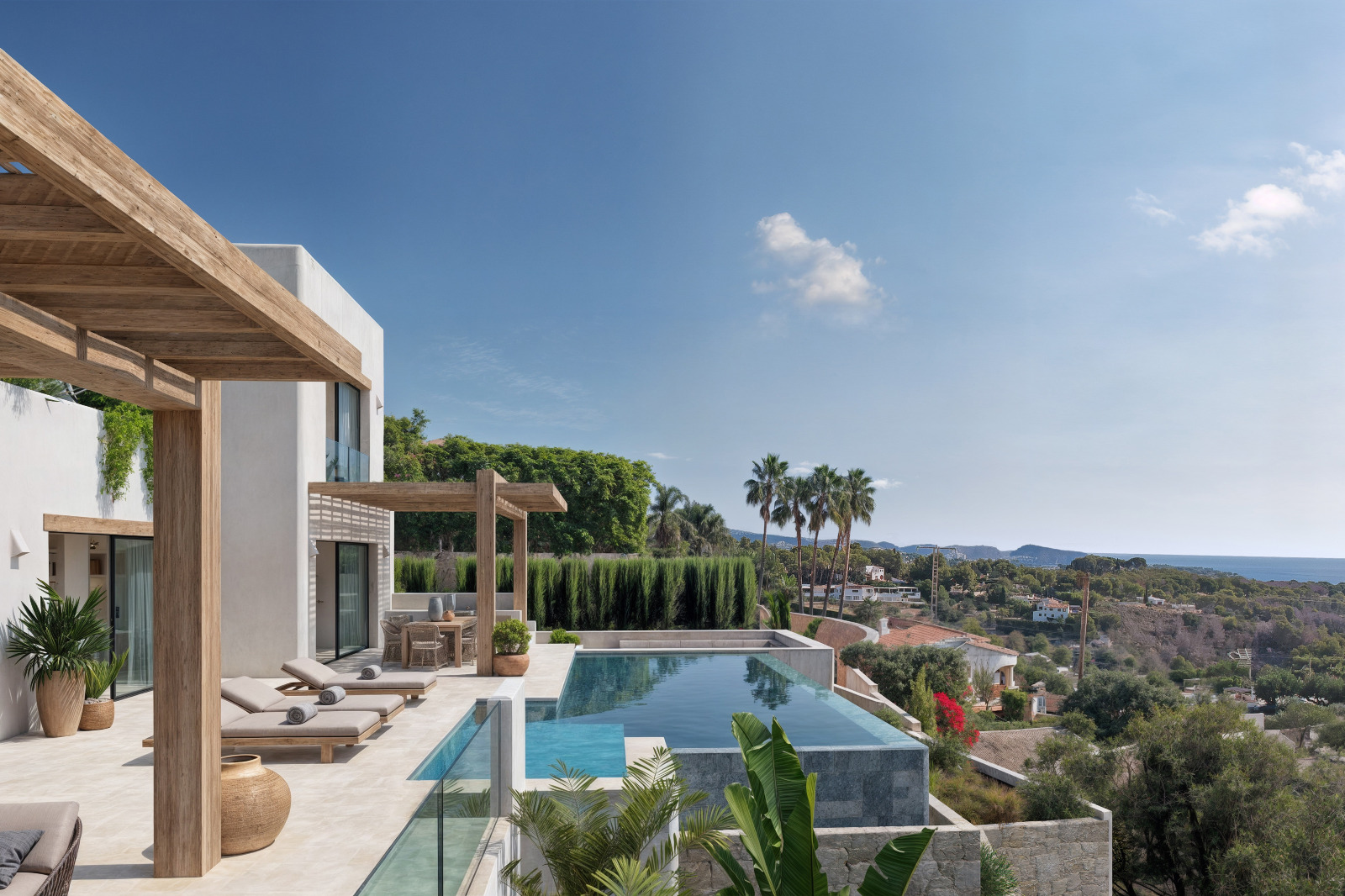 Buitenterras met overloopzwembad, houten pergola's en panoramisch uitzicht op zee. De witte gevel in Ibizastijl sluit aan bij de mediterrane beplanting.