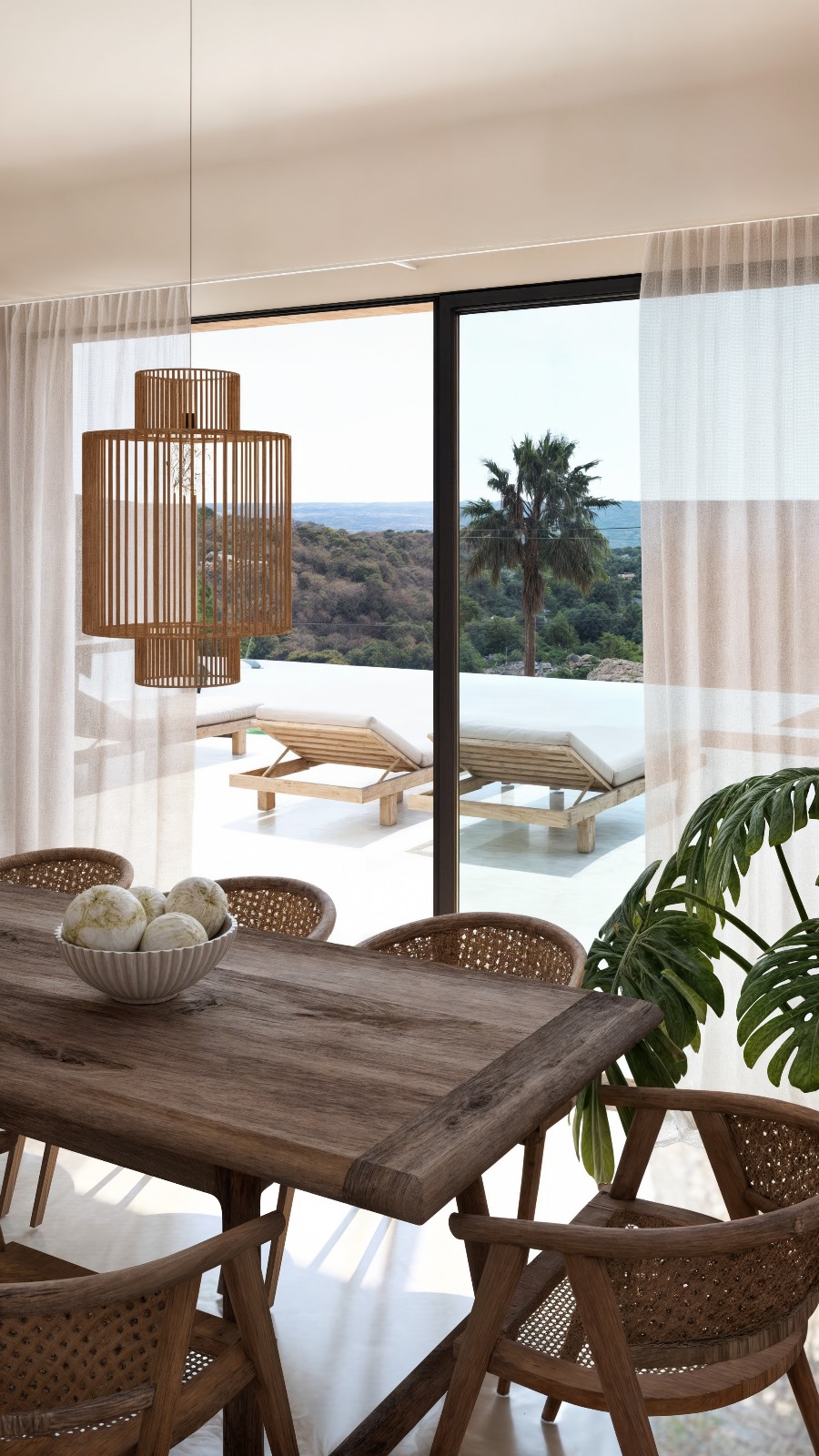 Eethoek met massief houten tafel en houten hanglamp, met uitzicht op het terras, infinity zwembad en de zee door grote glazen schuifdeuren.