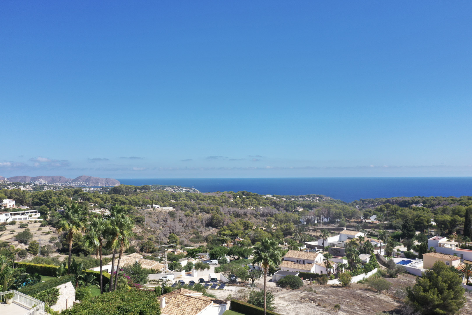 Verhoogd panoramisch uitzicht vanuit Racó de Galeno op de Middellandse Zee, met kustvegetatie en residentiële villa's in Benissa onder een heldere hemel.