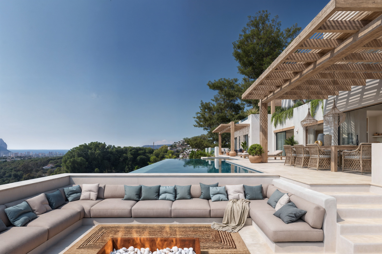 Verzonken buitenlounge met vuurplaats, houten pergola boven het terras en een overloopzwembad met panoramisch uitzicht op de Middellandse Zee en de Peñón de Ifach.