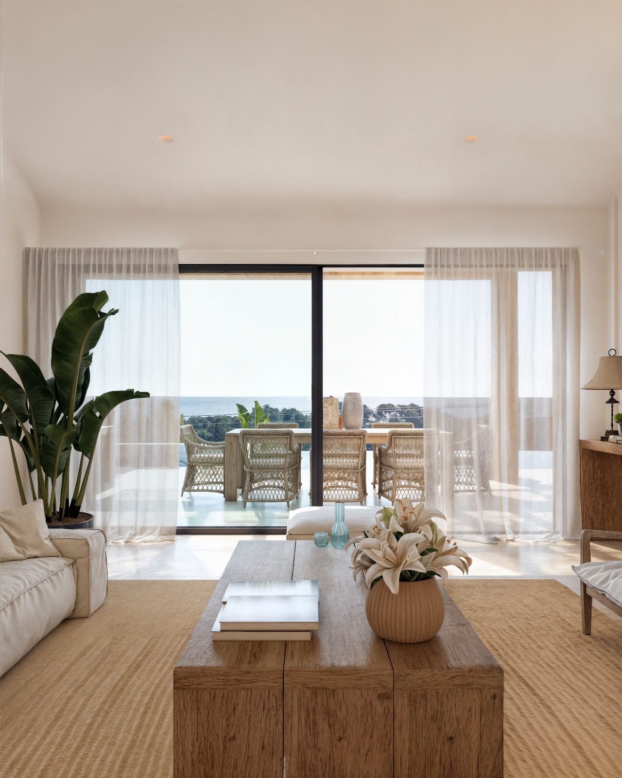 Woonkamer in Ibiza-stijl met een natuurhouten salontafel en grote schuifdeuren die toegang bieden tot een terras met eethoek en zeezicht.