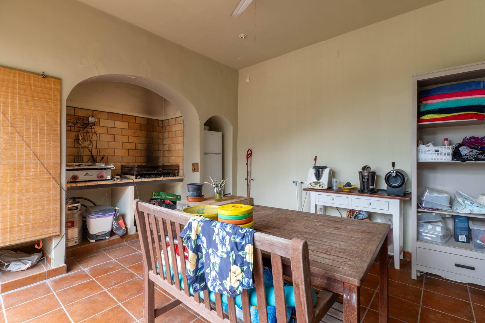 Buitenkeuken met een ingebouwde stenen barbecue, rustieke houten eettafel en authentieke terracotta vloertegels.