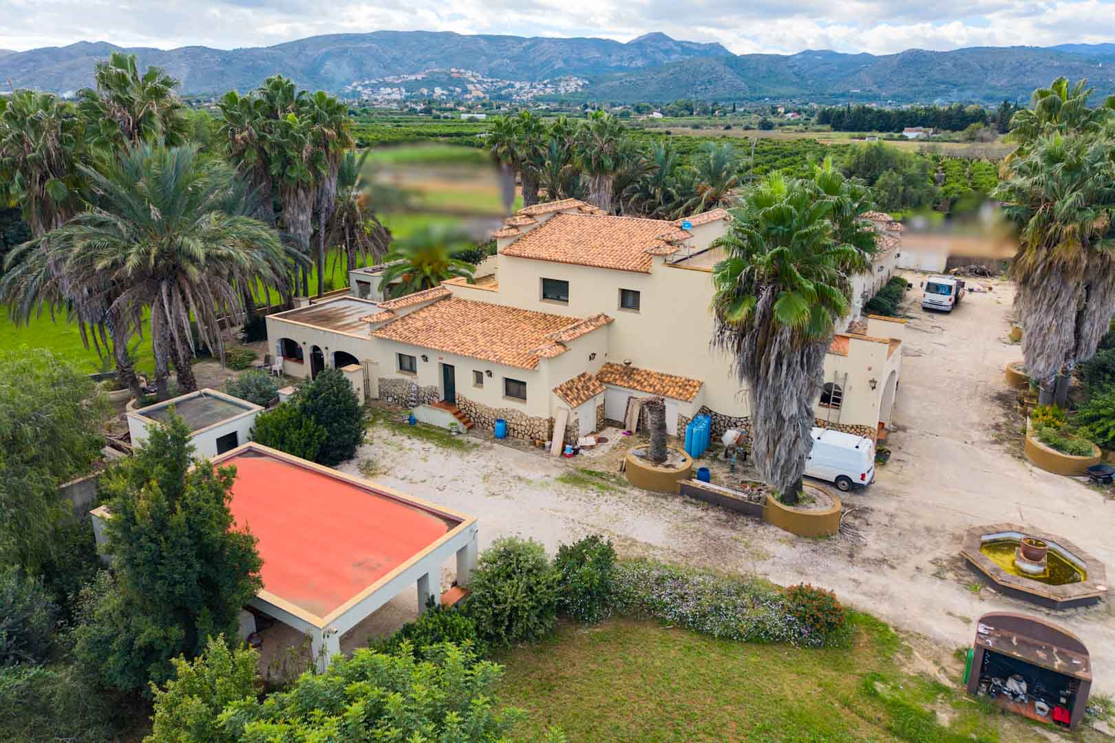 Luchtfoto van de mediterrane villa met terracotta daken, omgeven door palmbomen en tuinen, met panoramisch uitzicht op de vallei en de bergen.