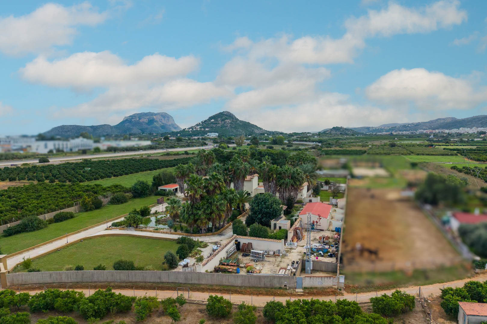 Luchtfoto van het landgoed van 10.000 m2 in Ondara, met uitgestrekte palmtuinen, een centrale vijver en weids uitzicht op de omliggende bergen.