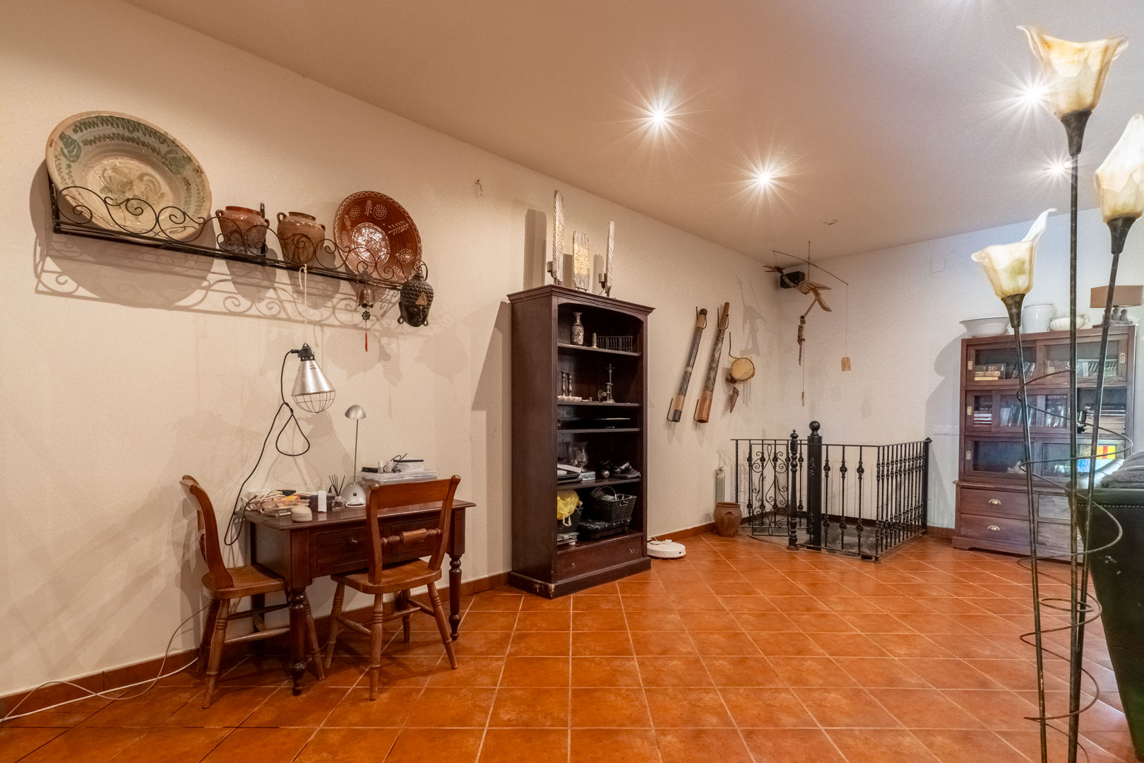 Werkruimte met houten bureau, terracotta tegelvloer en een smeedijzeren balustrade bij de trap naar de benedenverdieping.