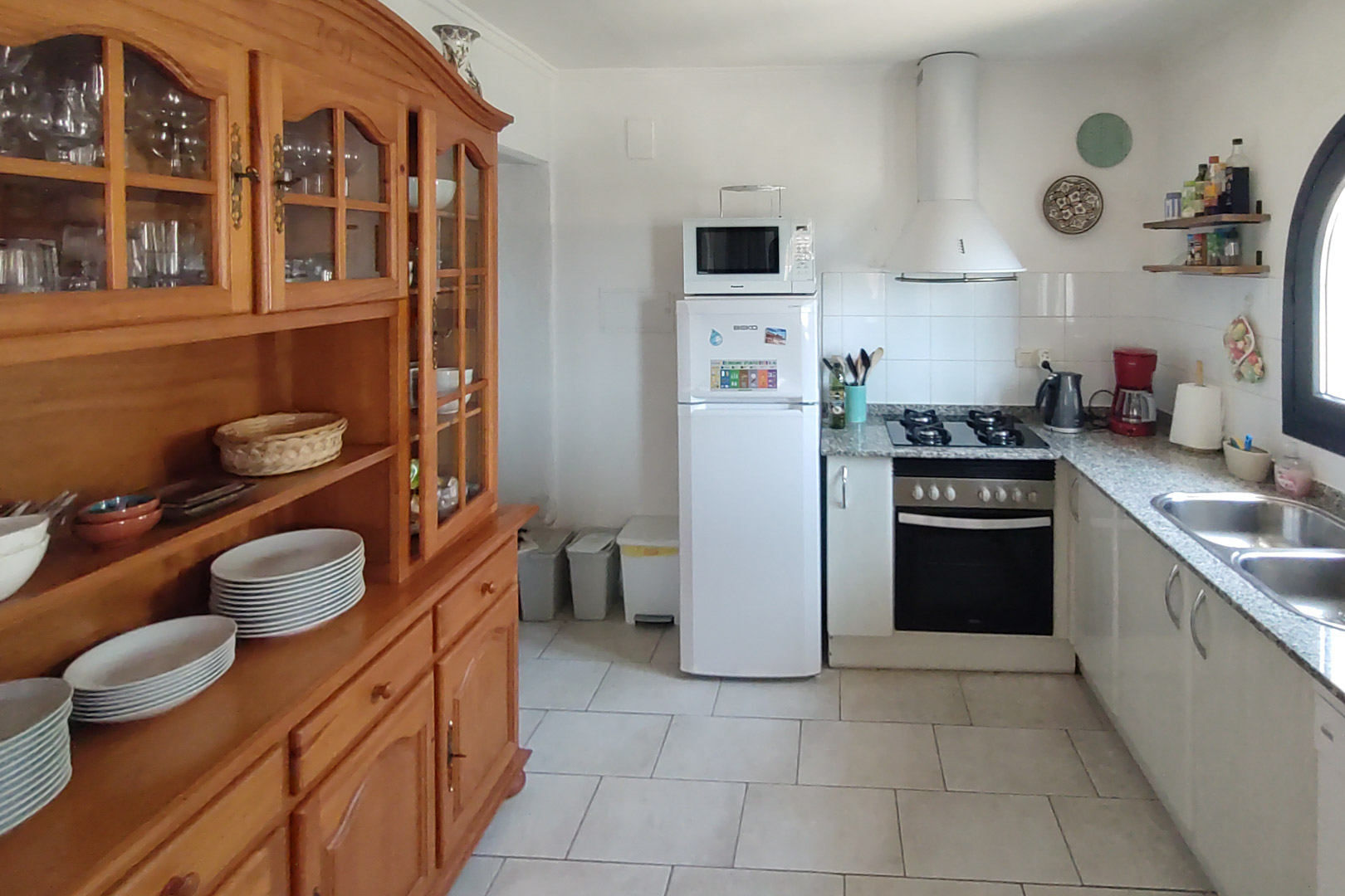 Functionele keuken met granieten werkblad, gaskookplaat en een grote massief houten servieskast op een lichte tegelvloer.