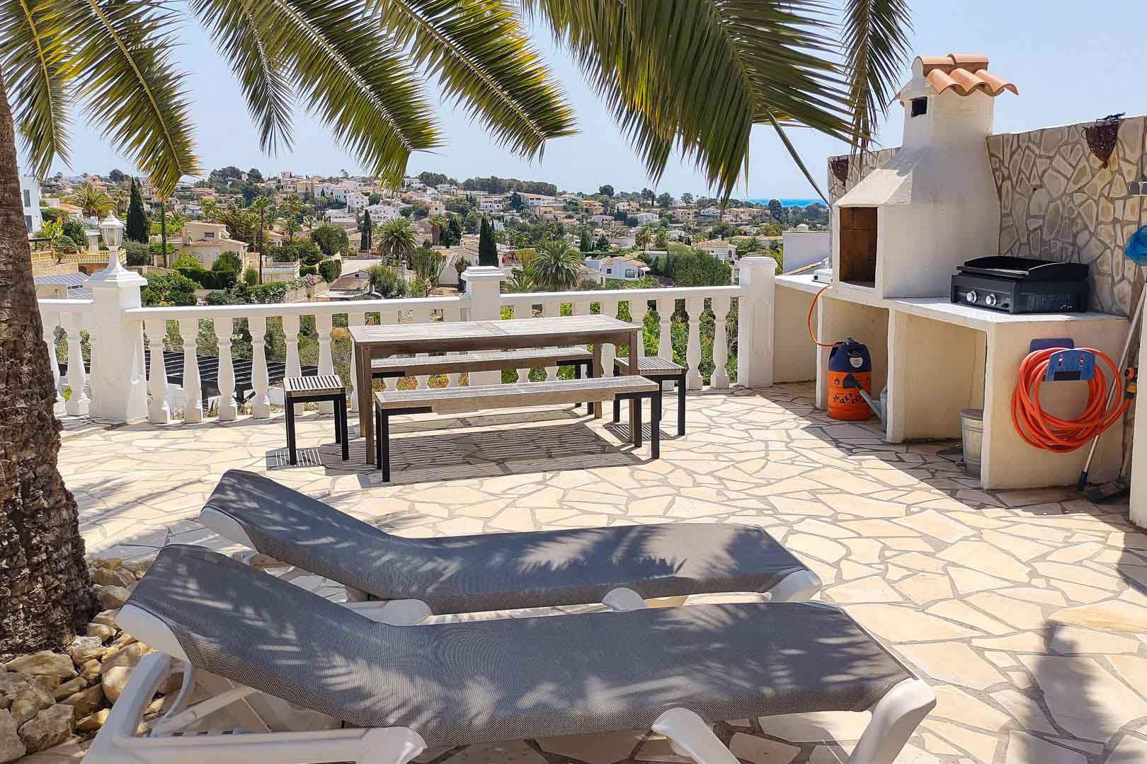 Met natuursteen geplaveid terras voorzien van een vaste barbecue, houten picknicktafel en ligbedden met uitzicht over de vallei en de zee.