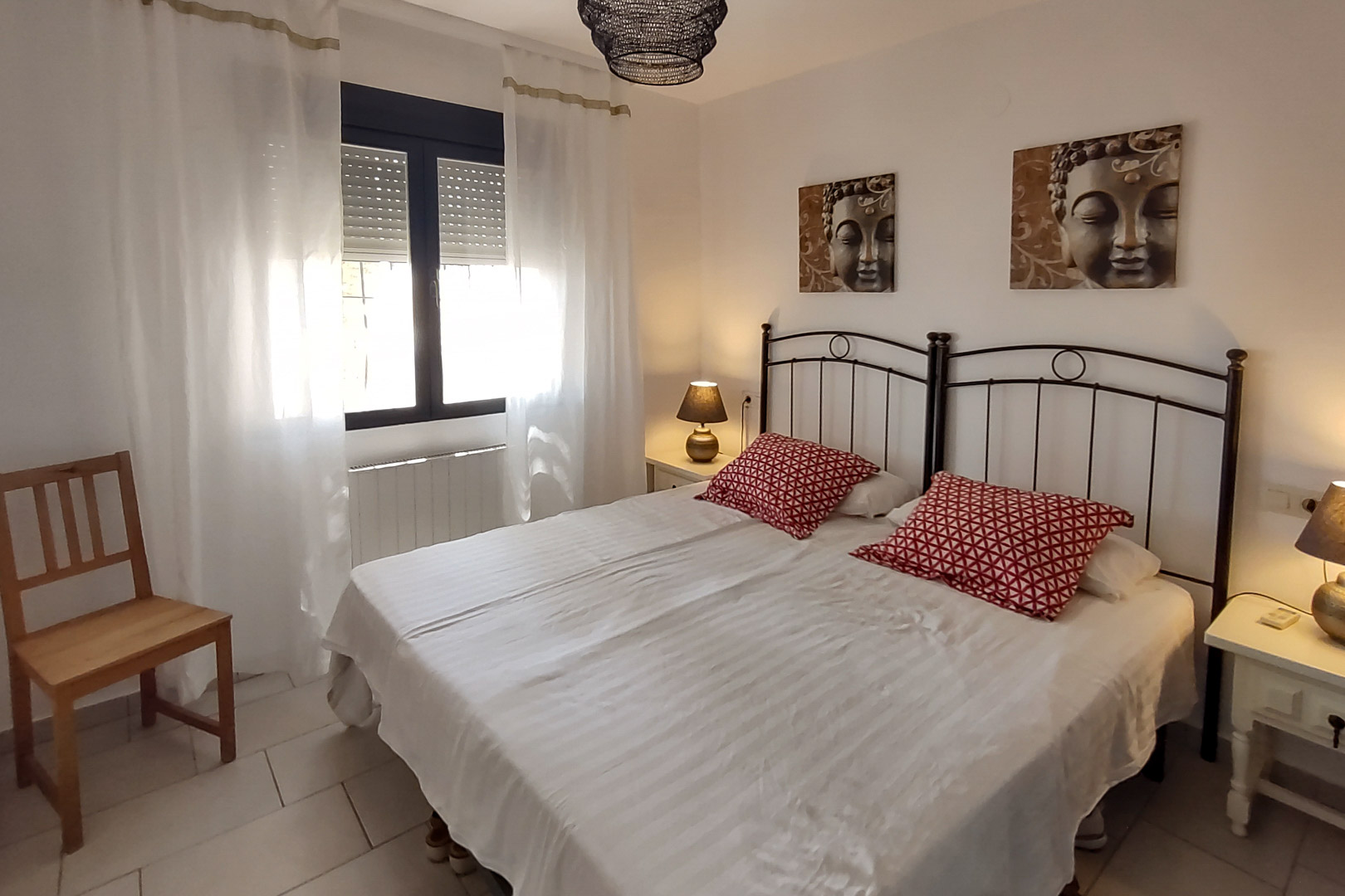 Slaapkamer met twee eenpersoonsbedden, zwart smeedijzeren hoofdeinden, Boeddha-schilderijen en raam met rolluiken en witte gordijnen.