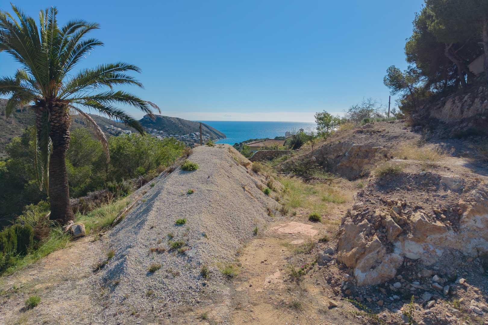 Hooggelegen perceel in Moraira met panoramisch uitzicht op de Middellandse Zee, omgeven door pijnbomen en natuurlijke rotsformaties.