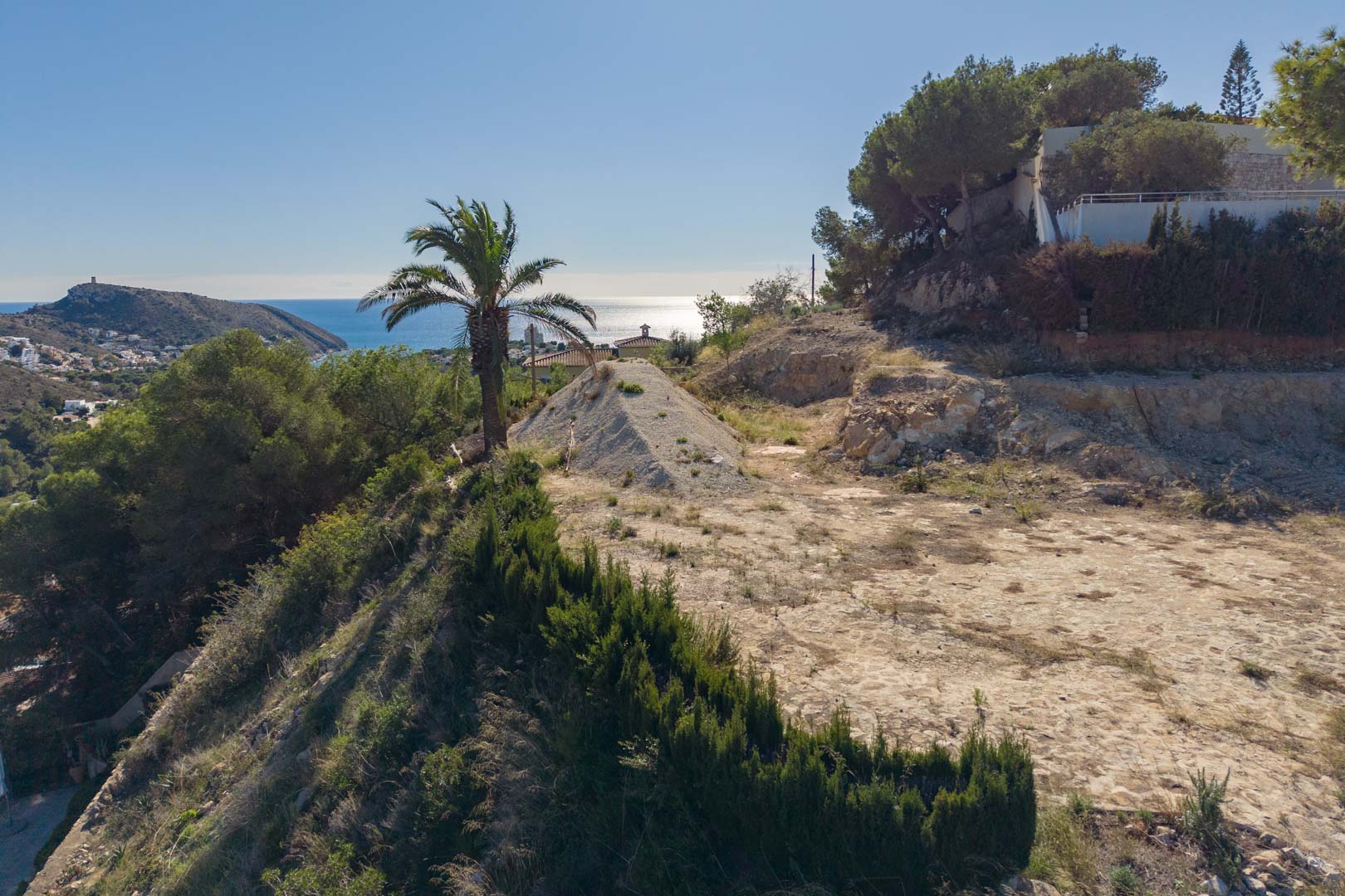 Verhoogd bouwperceel in Moraira met panoramisch uitzicht op de Middellandse Zee en El Portet, omgeven door pijnbomen en een natuurlijke omgeving.