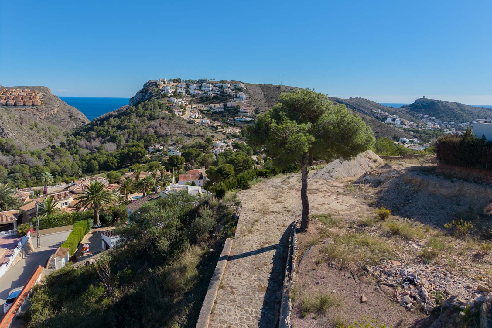 Verhoogd panoramisch uitzicht over de vallei van Moraira en de Middellandse Zee, omgeven door pijnbomen en een mediterraan heuvellandschap.
