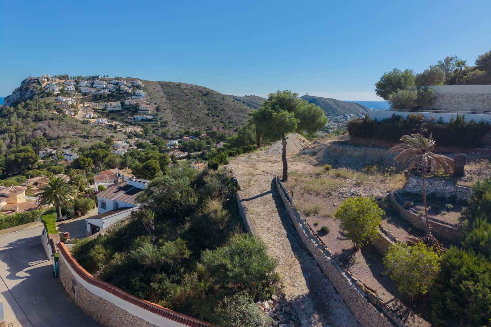 Verhoogd zicht op het perceel met natuurstenen muren en mediterrane vegetatie, met panoramisch uitzicht over de vallei en de zee in Moraira.