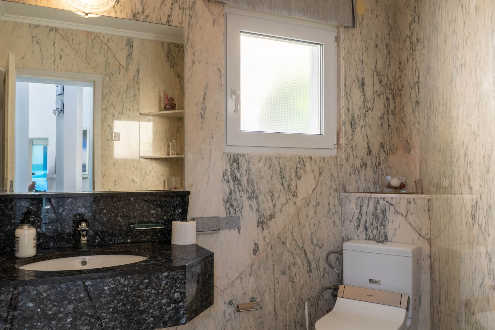 Badkamer met geaderde marmeren wanden en een zwart granieten aanrecht.