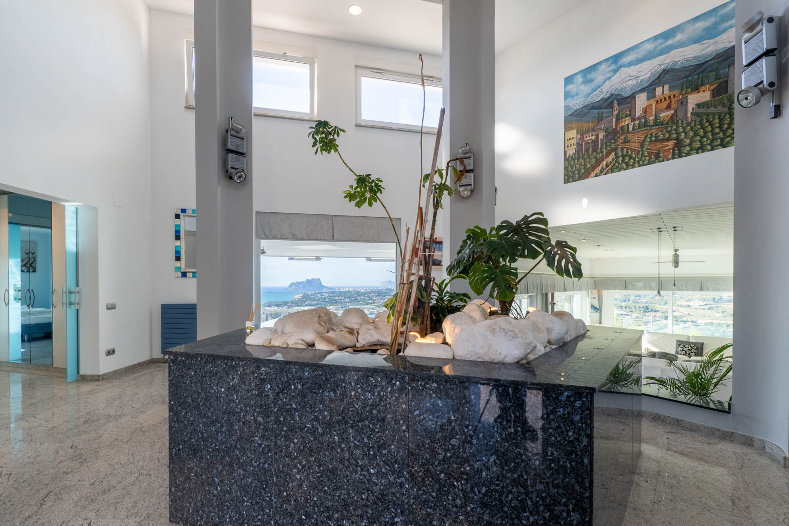 Interieurdetail met gepolijst granieten aanrecht, planten en uitzicht op de kust vanuit brede ramen.