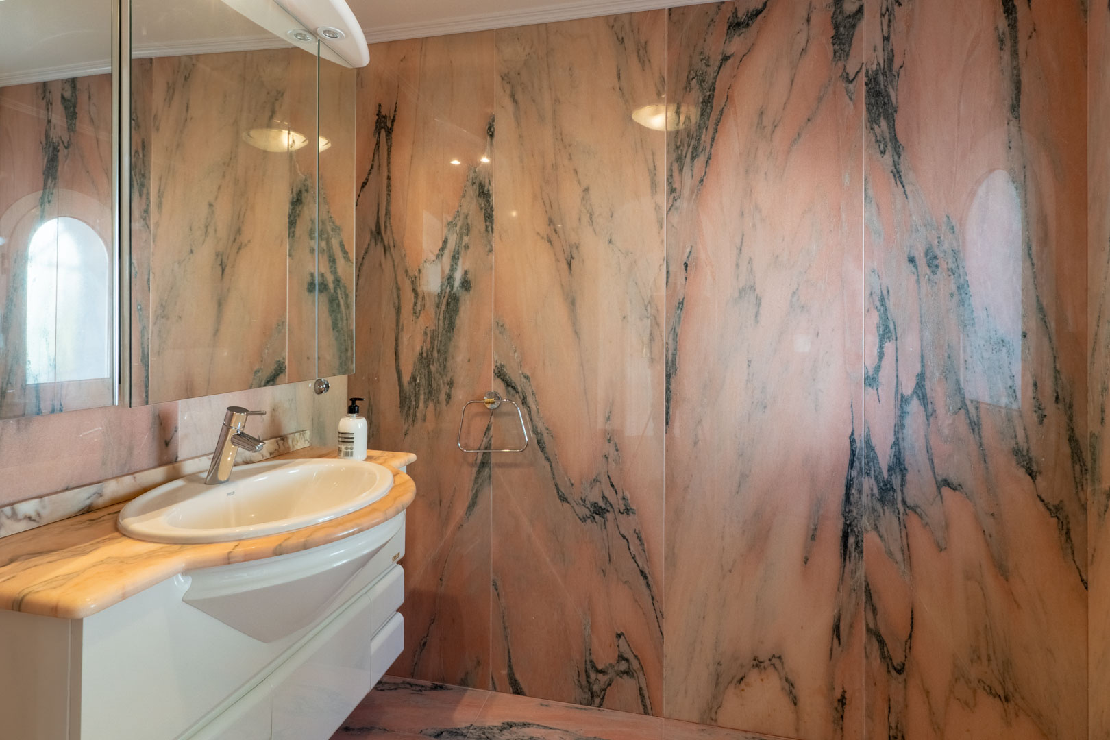Badkamer met volledige wandbekleding van roze marmer met donkere aders. Voorzien van een bijpassend stenen werkblad, wit wastafelmeubel en een grote spiegel.